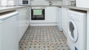 A compact kitchen with white cabinets, a microwave, an oven, and a washing machine. - Belfast Quarters: Modern City Centre Hub 3 Bed! (Belfast)