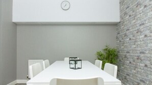 A conference room with a white table, six chairs, a clock on the wall, and a brick wall. - Belfast Quarters: Modern City Centre Hub 3 Bed! (Belfast)