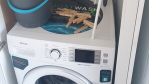 Een wasmachine met bedieningspaneel, een dweil, een emmer en een tuinslang.
