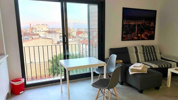 Een modern appartement met balkon, een eethoek, een bank en een schilderij aan de muur.
