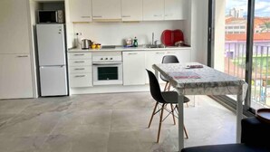 Een kleine keuken met witte kastjes, een inbouwoven en een eethoek met een tafel en stoelen.