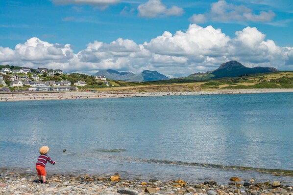 A coastal scene with a child playing near the water, houses in the background, and mountains in the distance.