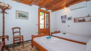 A room with two wooden beds, a stone floor, a wooden chair, a wooden table, and a ceiling with exposed beams.