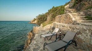 A seaside terrace with stone steps leading down to the water, equipped with lounge chairs and a table.