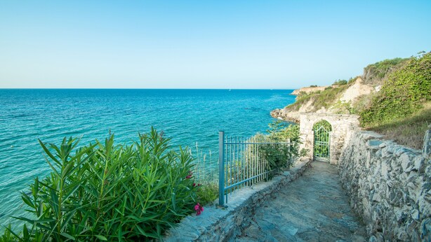 A coastal path leading to a stone archway overlooking the sea.