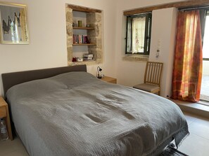 A bedroom with a bed, a nightstand, a chair, a bookshelf, and a window with curtains. - Finika House & Garden - Traditional charm with modern comfort. Vori, South Crete (Vori)