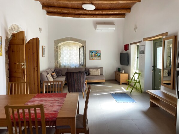 A cozy living room with a wooden ceiling, a sofa, a dining table with chairs, and a TV. - Finika House & Garden - Traditional charm with modern comfort. Vori, South Crete (Vori)