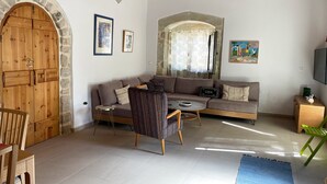 Un salon avec une porte en arc de pierre, un canapé, un fauteuil à motifs, une petite table et un téléviseur.