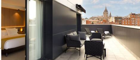 Una habitación de hotel moderna con balcón, cama y zona de estar con sillas y una mesa.