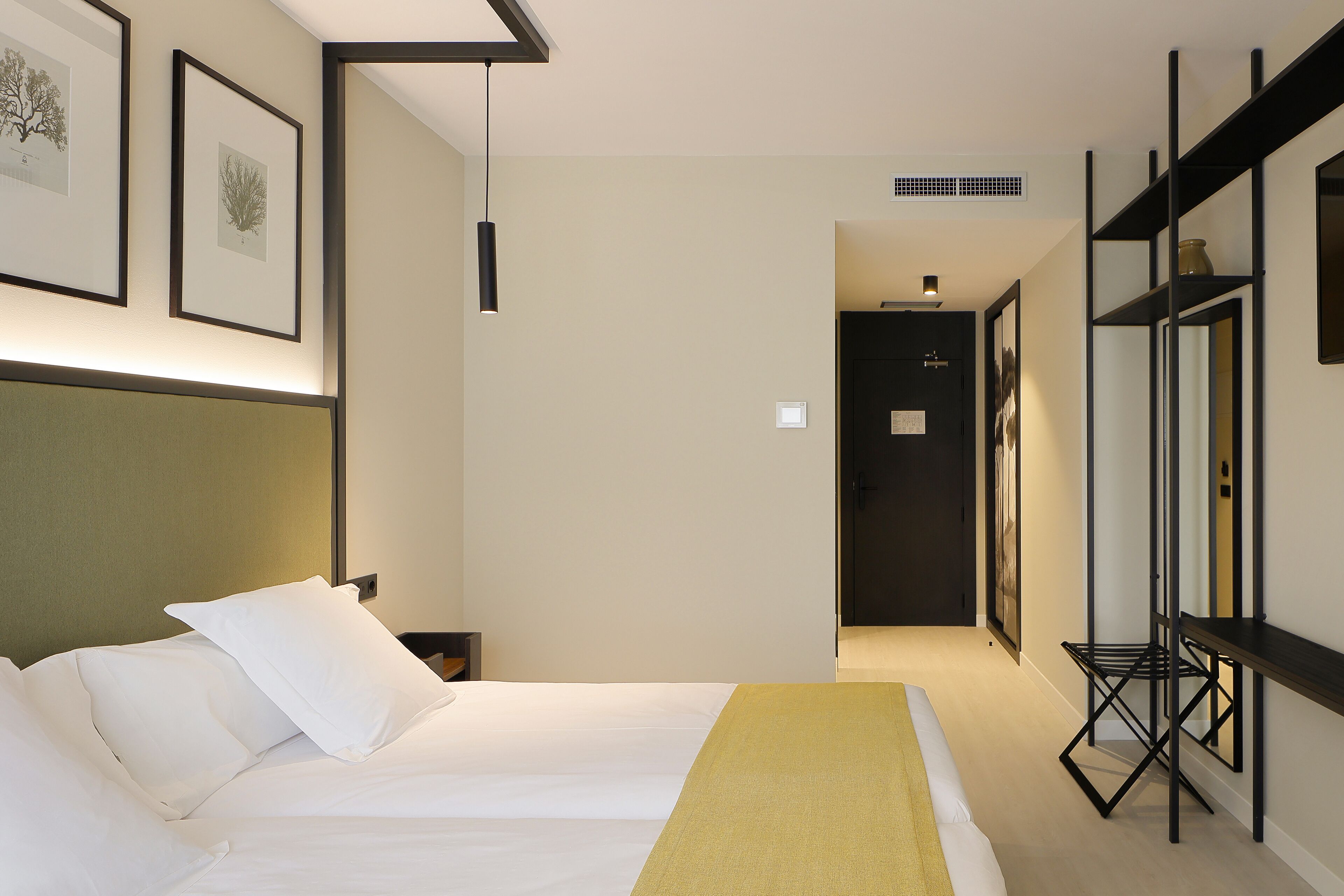 A hotel room with a bed, bedside tables, a desk, and a chair. There is a door leading to another room.