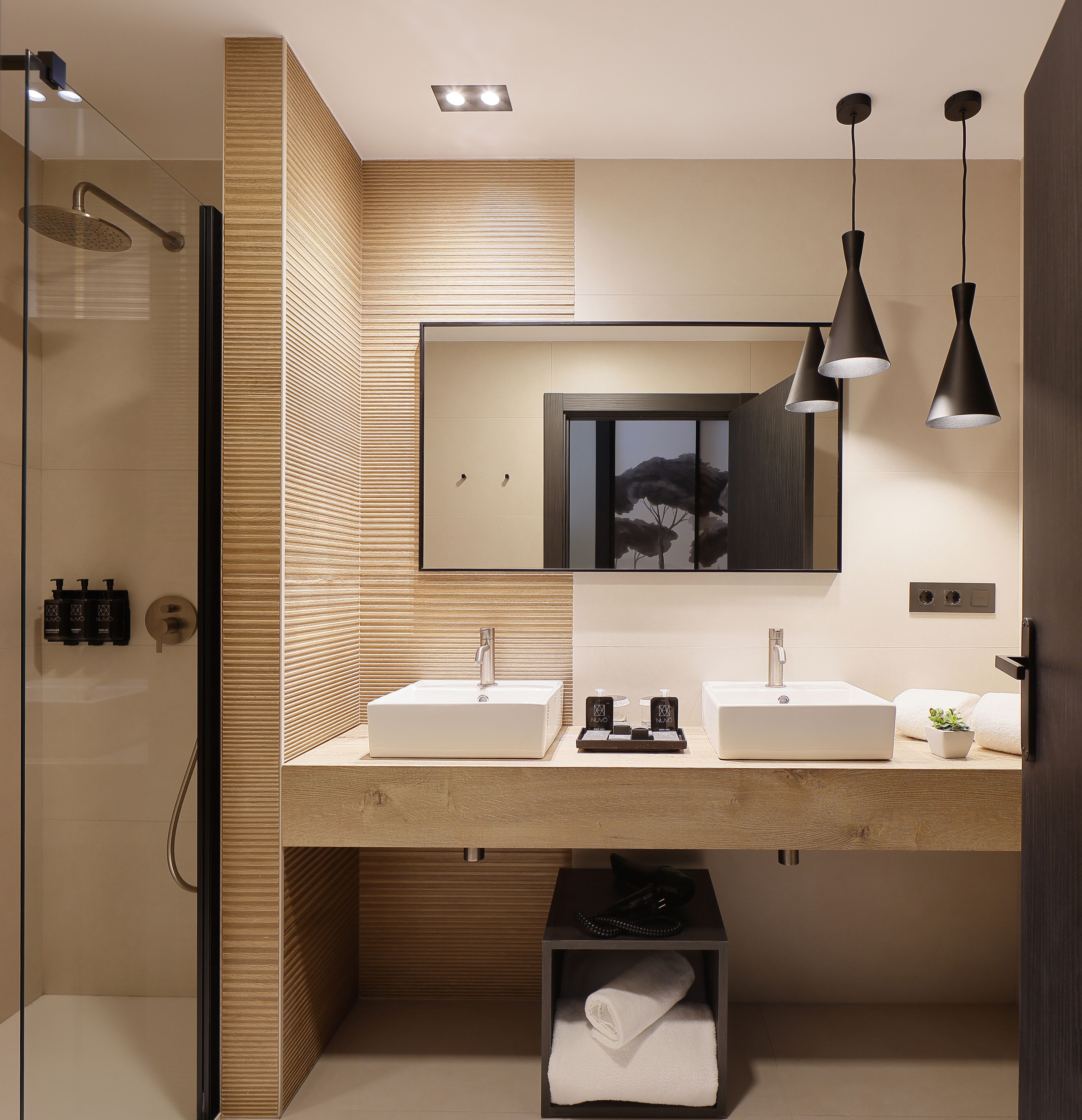 A modern bathroom with a walk-in shower, two sinks, a mirror, pendant lights, and a towel rack.