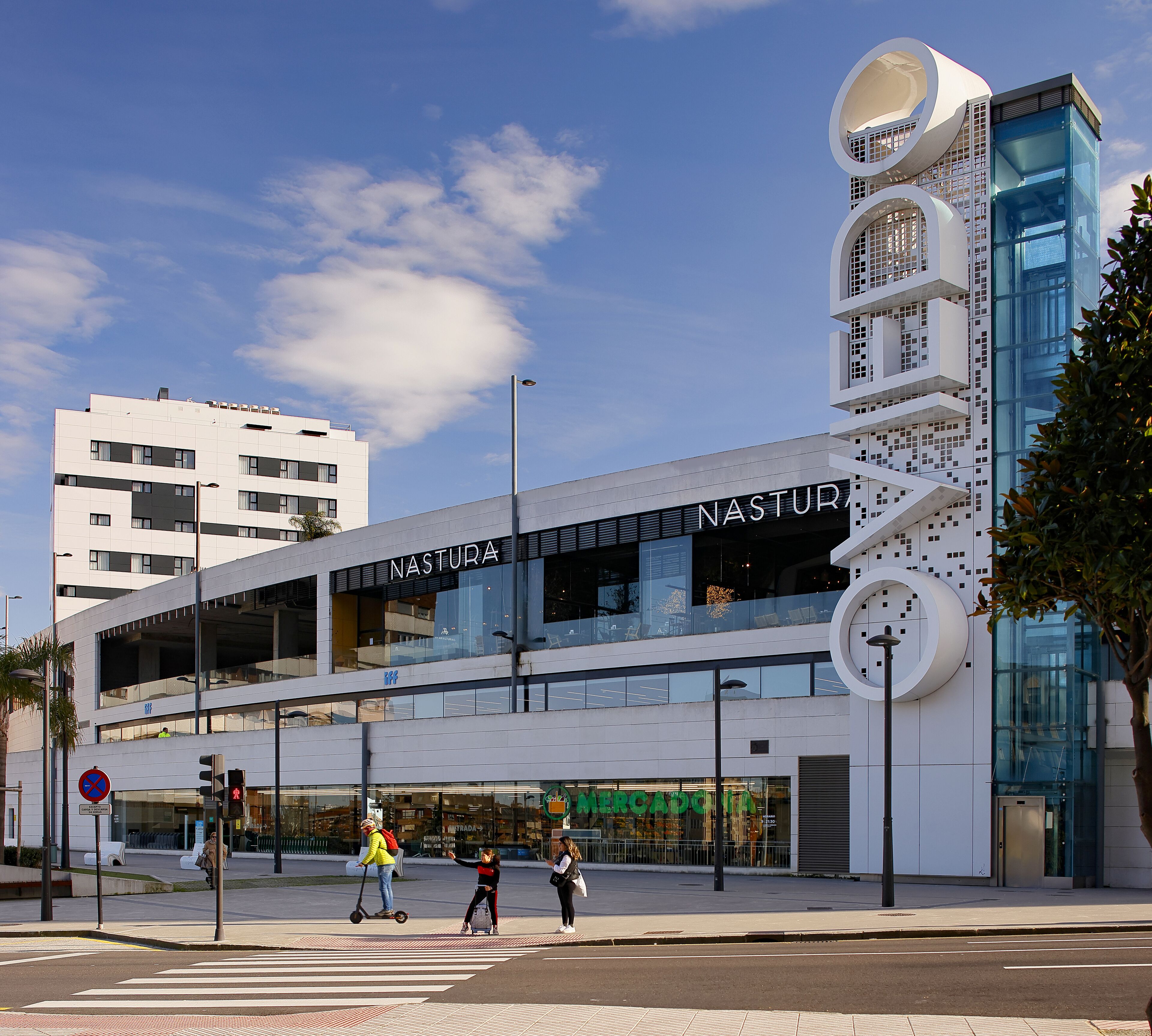 Un edificio moderno con un llamativo letrero 'NASTURA', que destaca por su diseño arquitectónico único con elementos circulares y fachada de vidrio.
