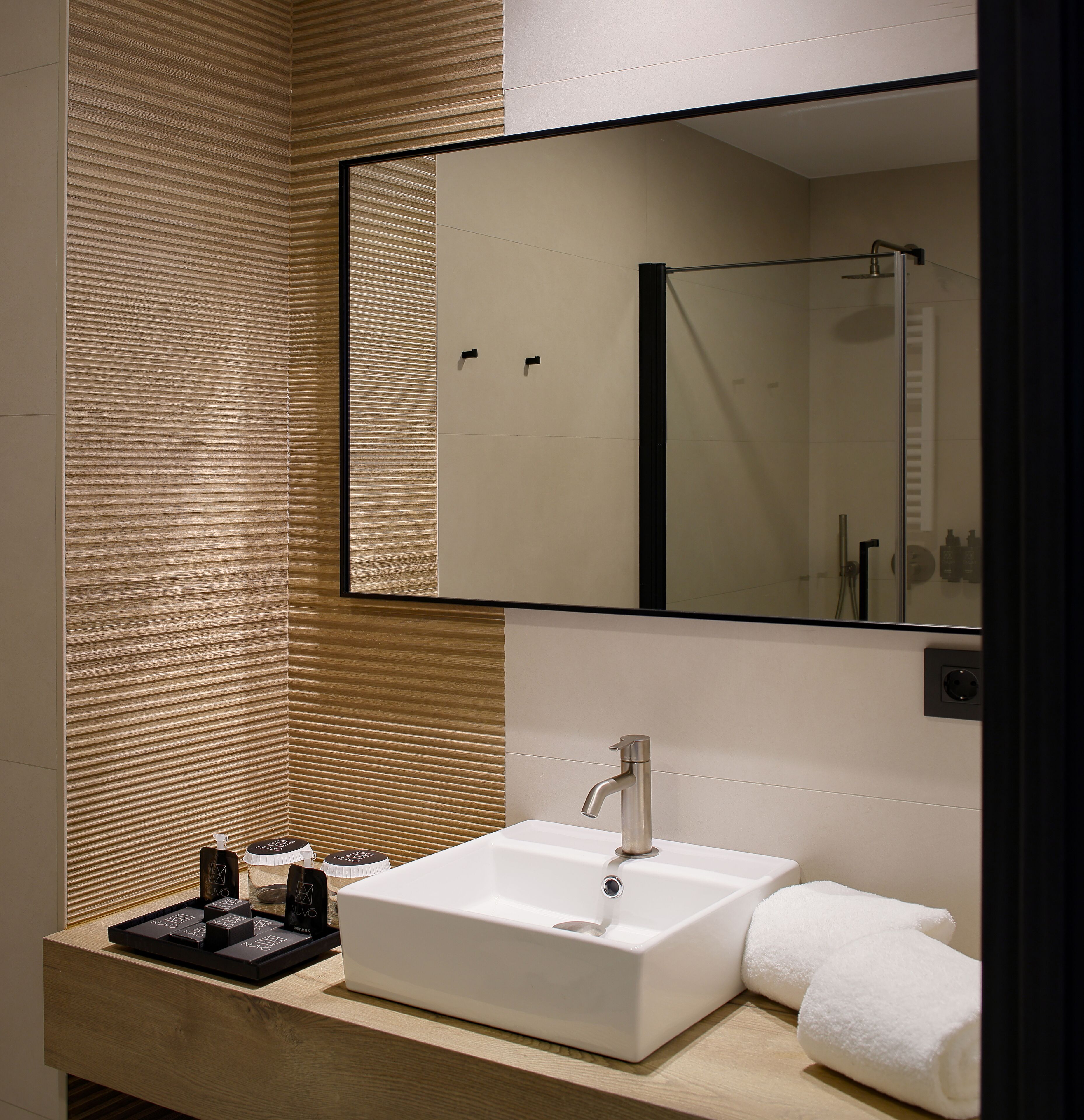 A modern bathroom with a large mirror, a white sink, and a towel.