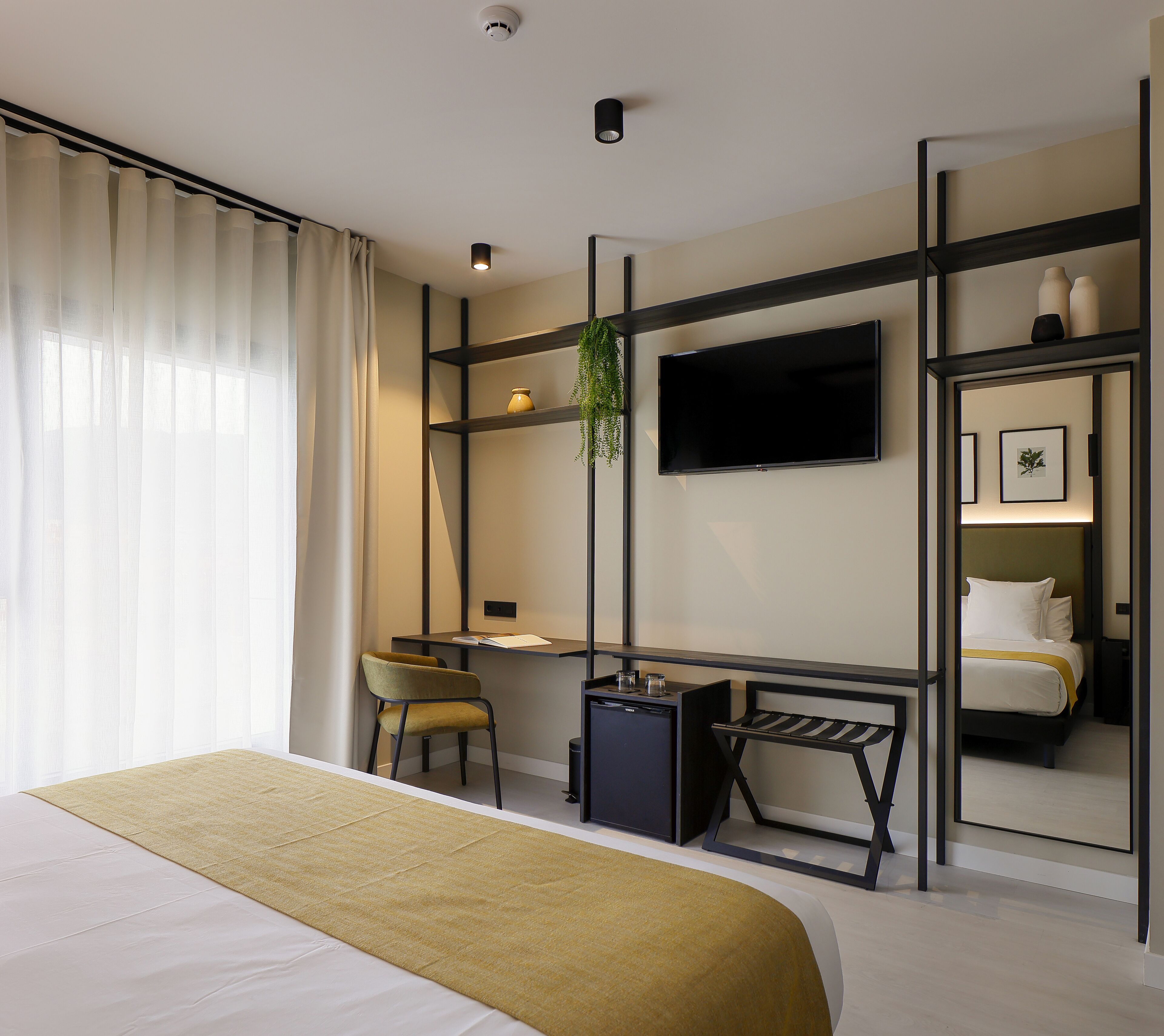 Una habitación de hotel moderna con cama, escritorio, silla, televisor y espejo.