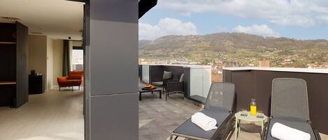 Un balcón con dos sillones de relax, una mesita y vistas a un pueblo y colinas a lo lejos.