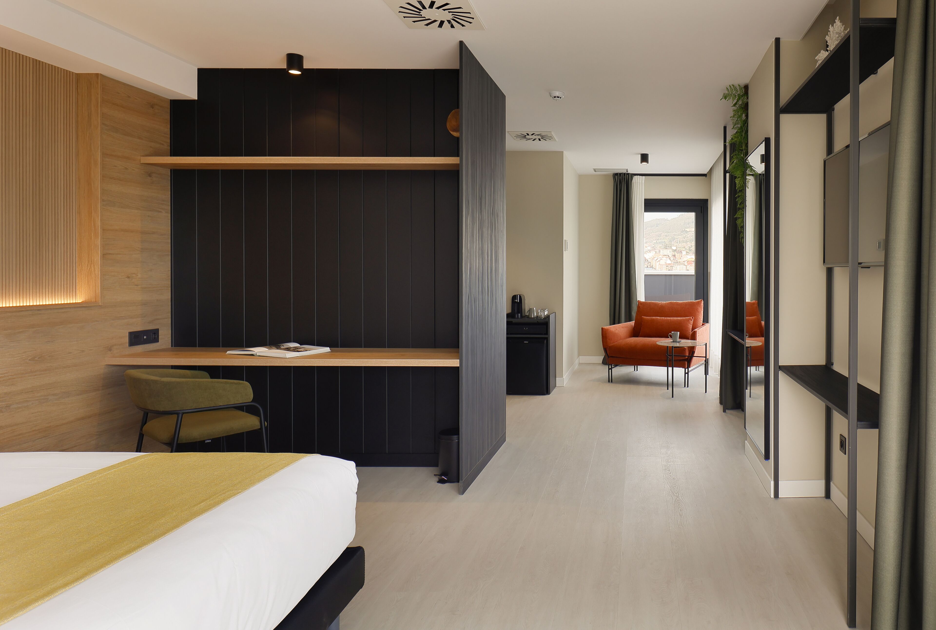 A modern hotel room with a bed, desk, and seating area.