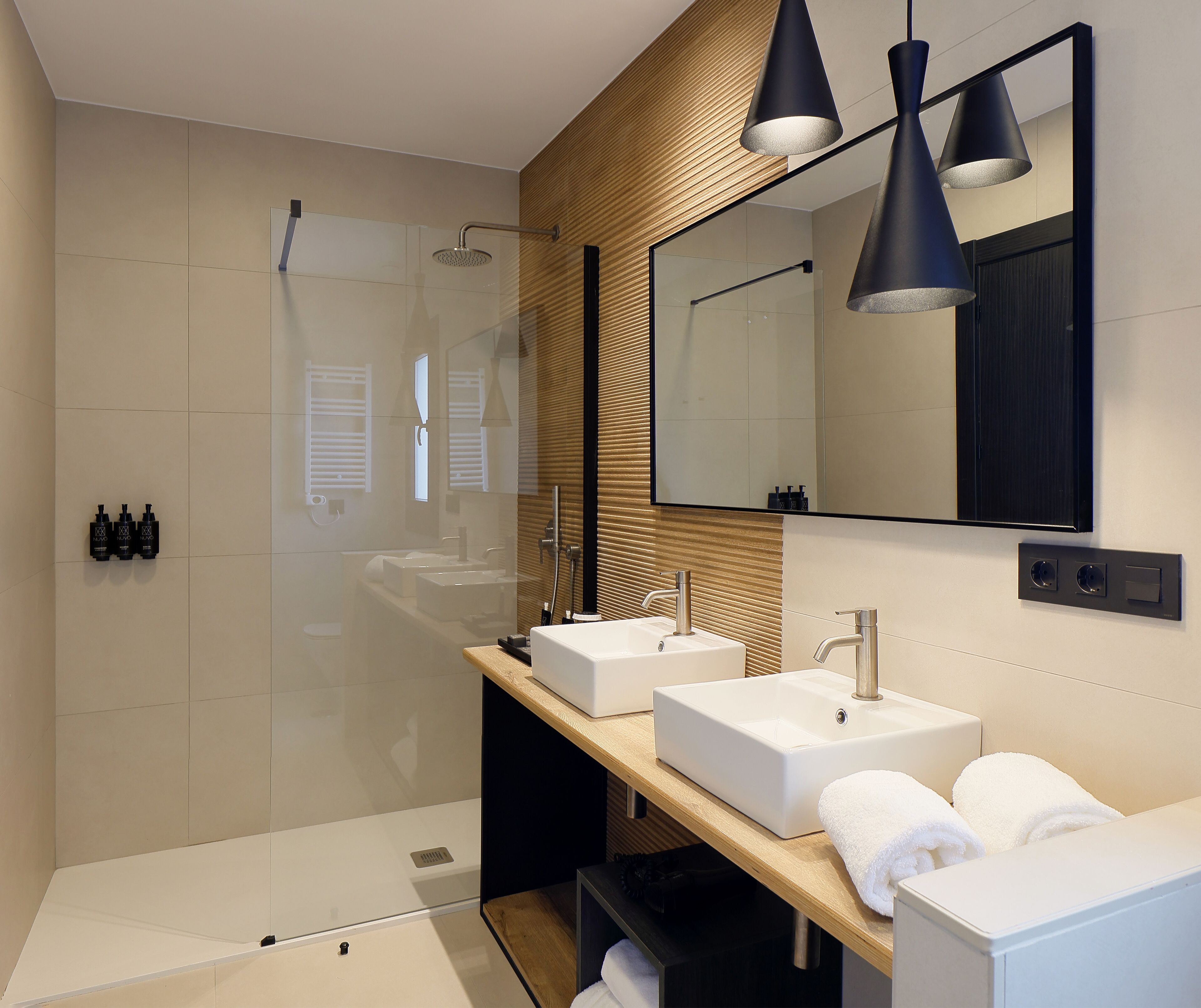 A modern bathroom with two sinks, a shower, and a large mirror.