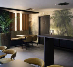 A modern interior with a dining area, a large potted plant, and a mural of palm trees. - NUVÓ HOTEL BOUTIQUE (Oviedo)