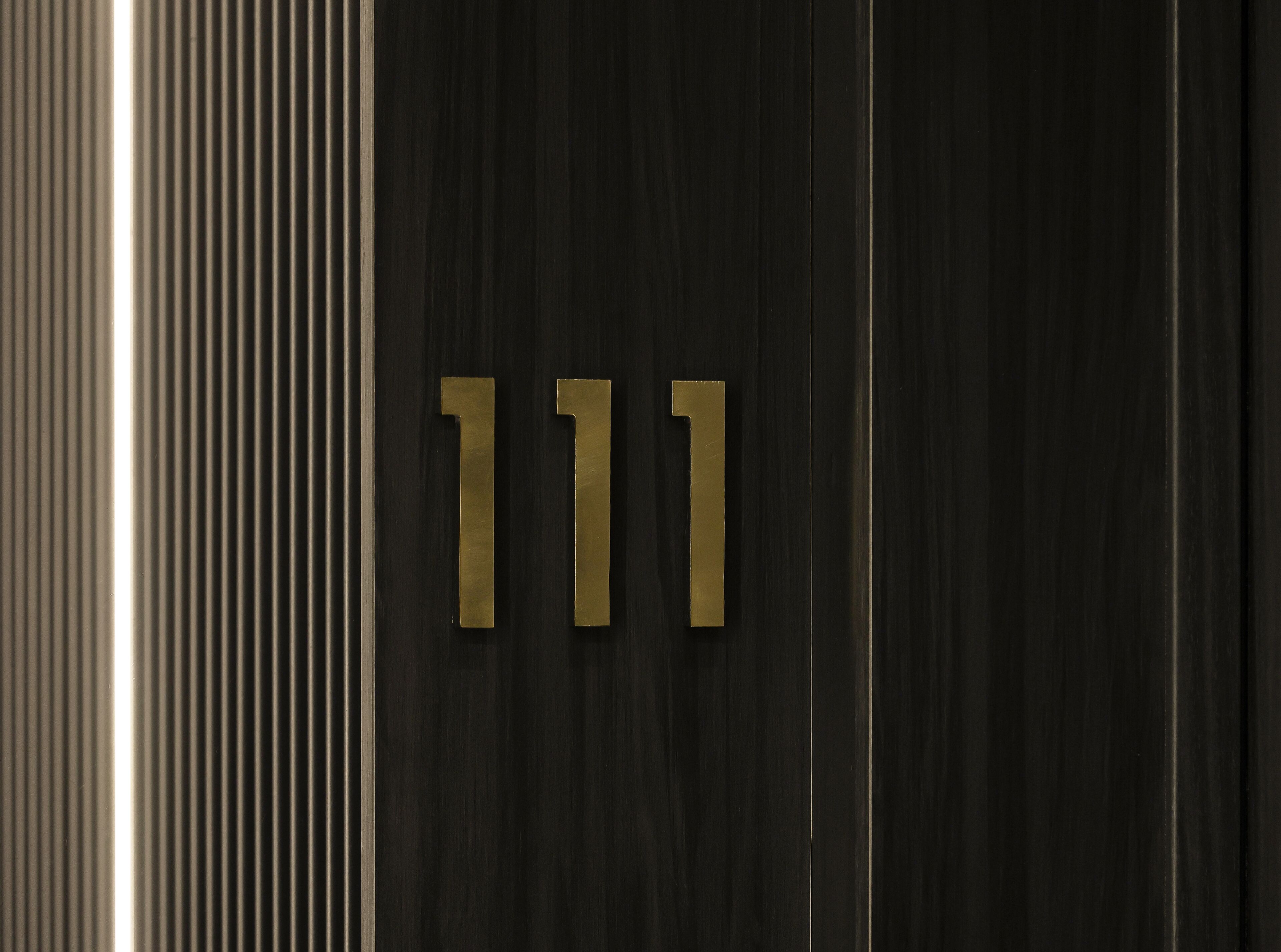 A close-up of a dark wood panel with two brass numbers '111' mounted on it.