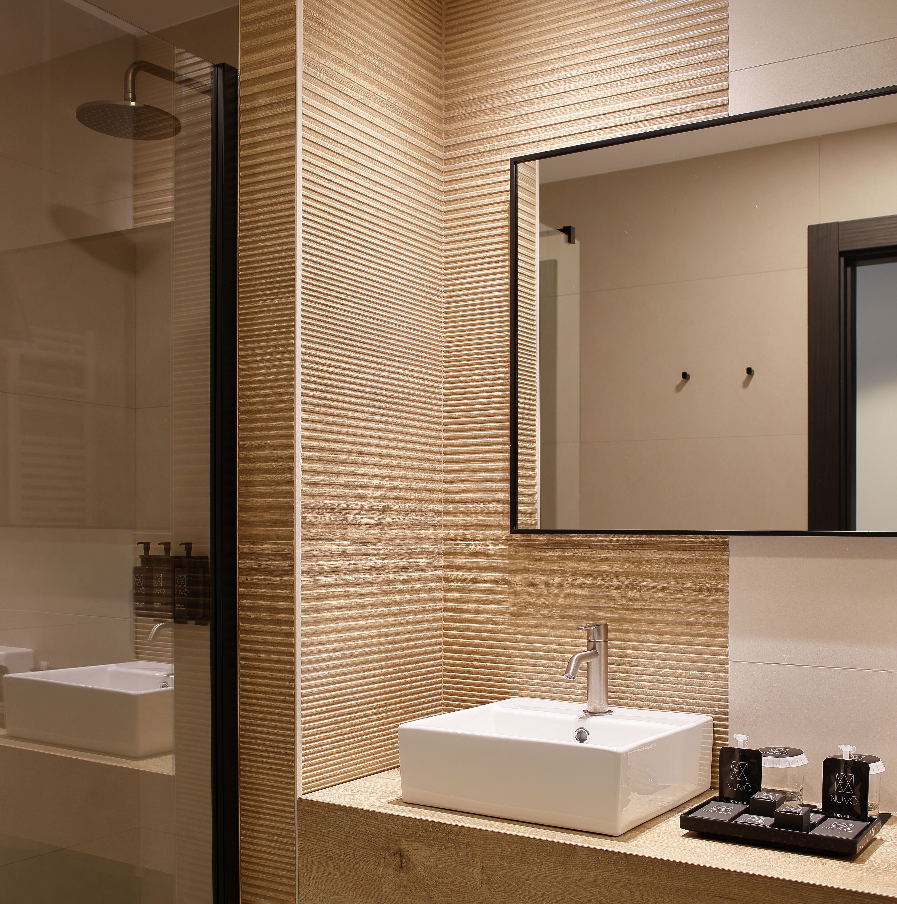 Un baño moderno con un espejo grande, un lavamanos blanco y una zona de ducha.