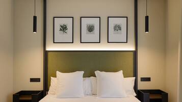 A hotel room with a large bed, three framed botanical prints on the wall, and two bedside tables with lamps.
