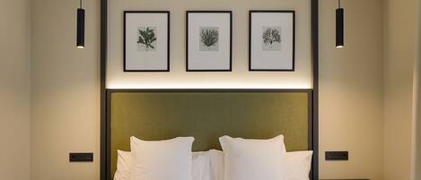 Habitación de hotel con una cama grande, tres láminas botánicas enmarcadas en la pared y dos mesitas de noche con lámparas.