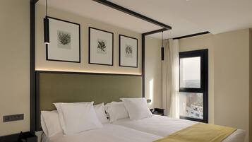 Una habitación de hotel con una cama grande, cabecera, ventana con cortinas e impresiones botánicas enmarcadas en la pared.