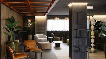 A modern lobby with a wooden ceiling, a large potted plant, leather chairs, a round coffee table, and a tall black shelving unit.