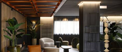 Un hall d’entrée moderne avec un plafond en bois, une grande plante en pot, des fauteuils en cuir, une table basse ronde et une grande étagère noire.