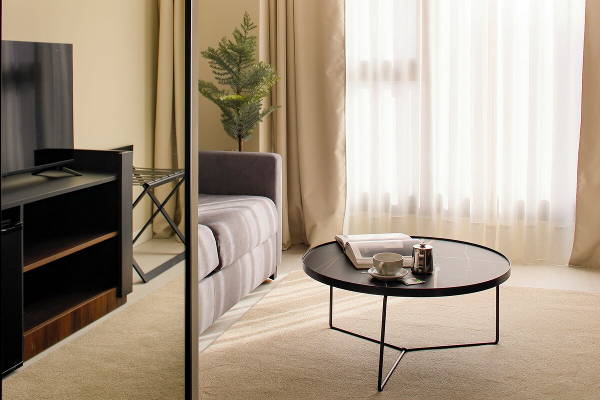 A hotel room with a bed, a TV, a coffee table, and a plant.