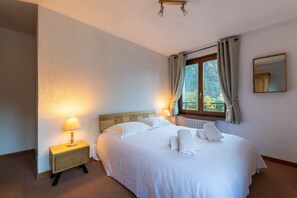 A hotel room with a large bed, a bedside lamp, a window with curtains, and a radiator.