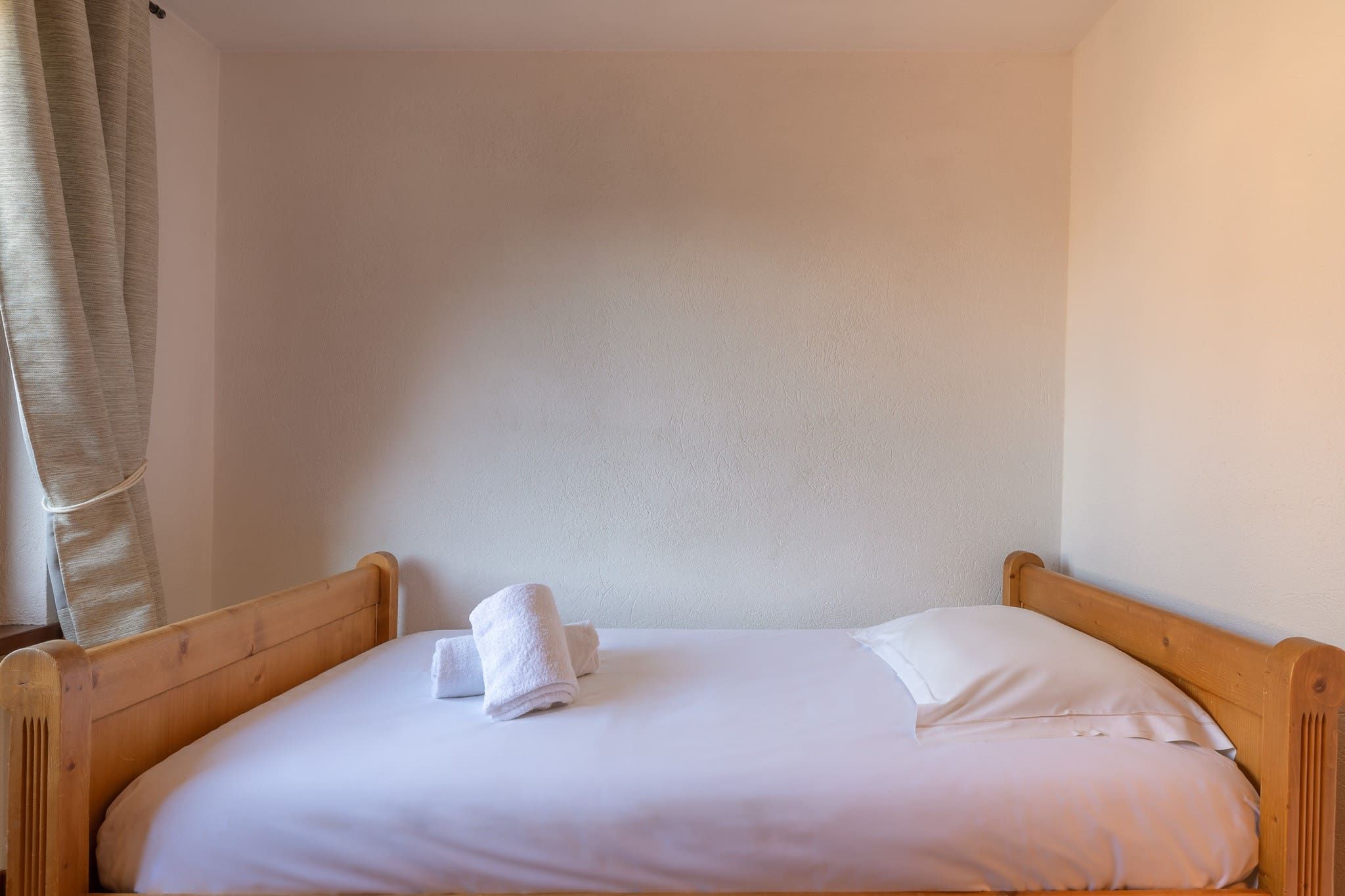Un lit simple avec une tête de lit et un pied de lit en bois, une literie blanche et une serviette blanche pliée posée sur le lit.
