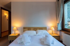 Habitació d'hotel amb un llit, dues làmpades de nit, una finestra amb cortines i vista a edificis.