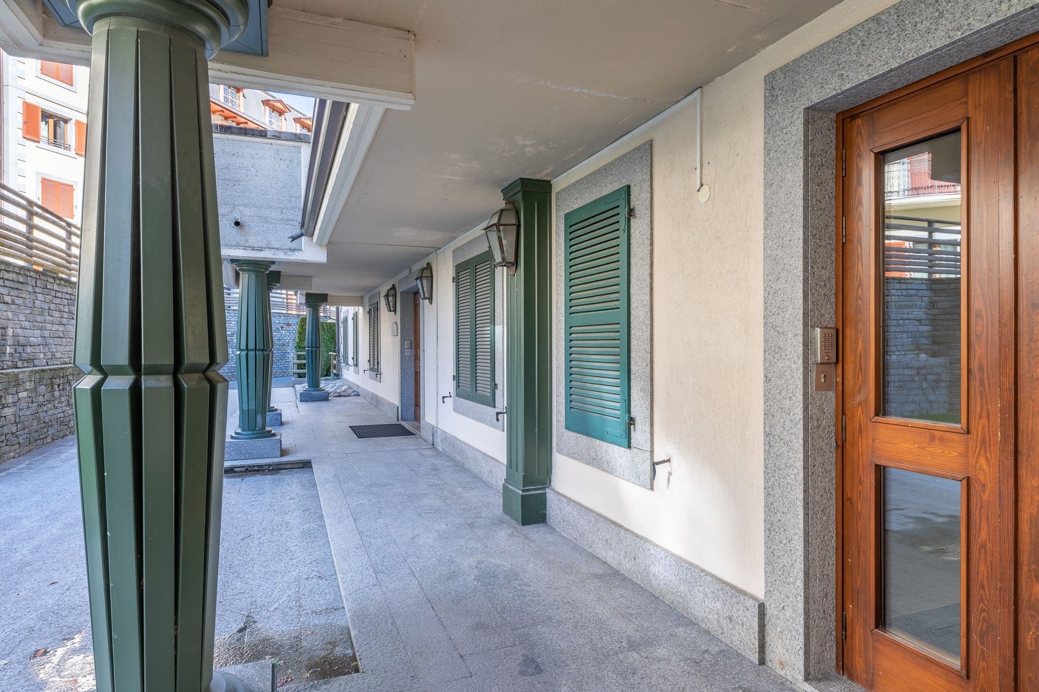 Un couloir extérieur abrité, doté de volets verts, d’une porte en bois et d’un mur en pierre.