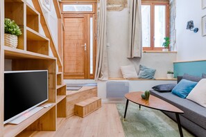 Moderni olohuone, jossa on litteänäyttöinen televisio, puuhyllyt, koristetyynyillä varustettu sohva, pieni p öytä ja ikkuna, jossa on verhot.