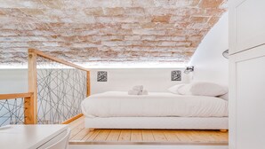 A loft bedroom with a wooden floor, white bed, and a view of the sky through a skylight. - Smartstay Louis Chazette - Centre-ville (Lyon)