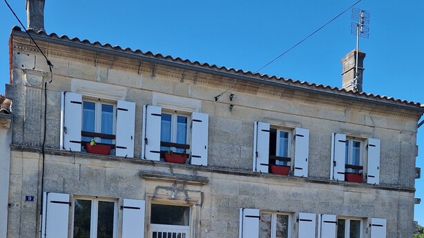 A two-story stone building with white shutters, a central entrance with a door, and multiple windows with shutters. - Gîte Padura - Location 3 Chambres - Braud et Saint Louis (Braud-et-Saint-Louis)