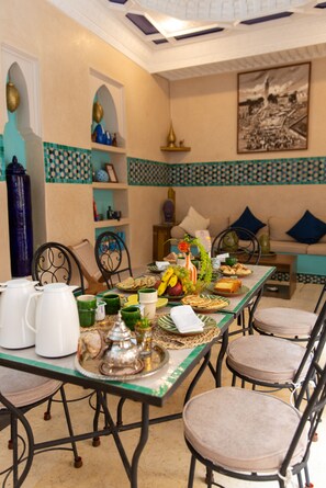 A dining area with a long table set for a meal, chairs, a sofa, and decorative items. - Riad La Rose Orientale Marrakech (Marrakech)
