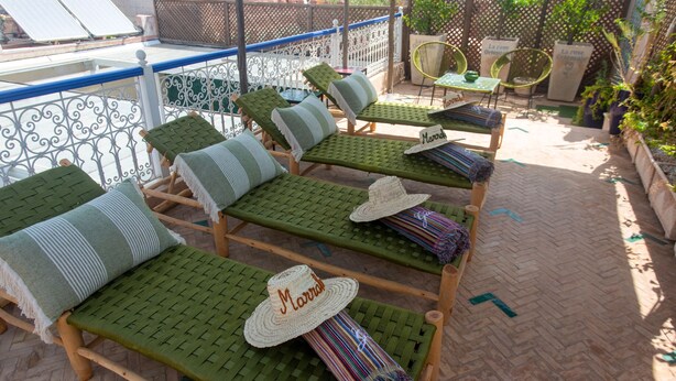 A rooftop terrace with multiple lounge chairs, each with a woven seat and backrest, and a hat placed on one of the chairs.