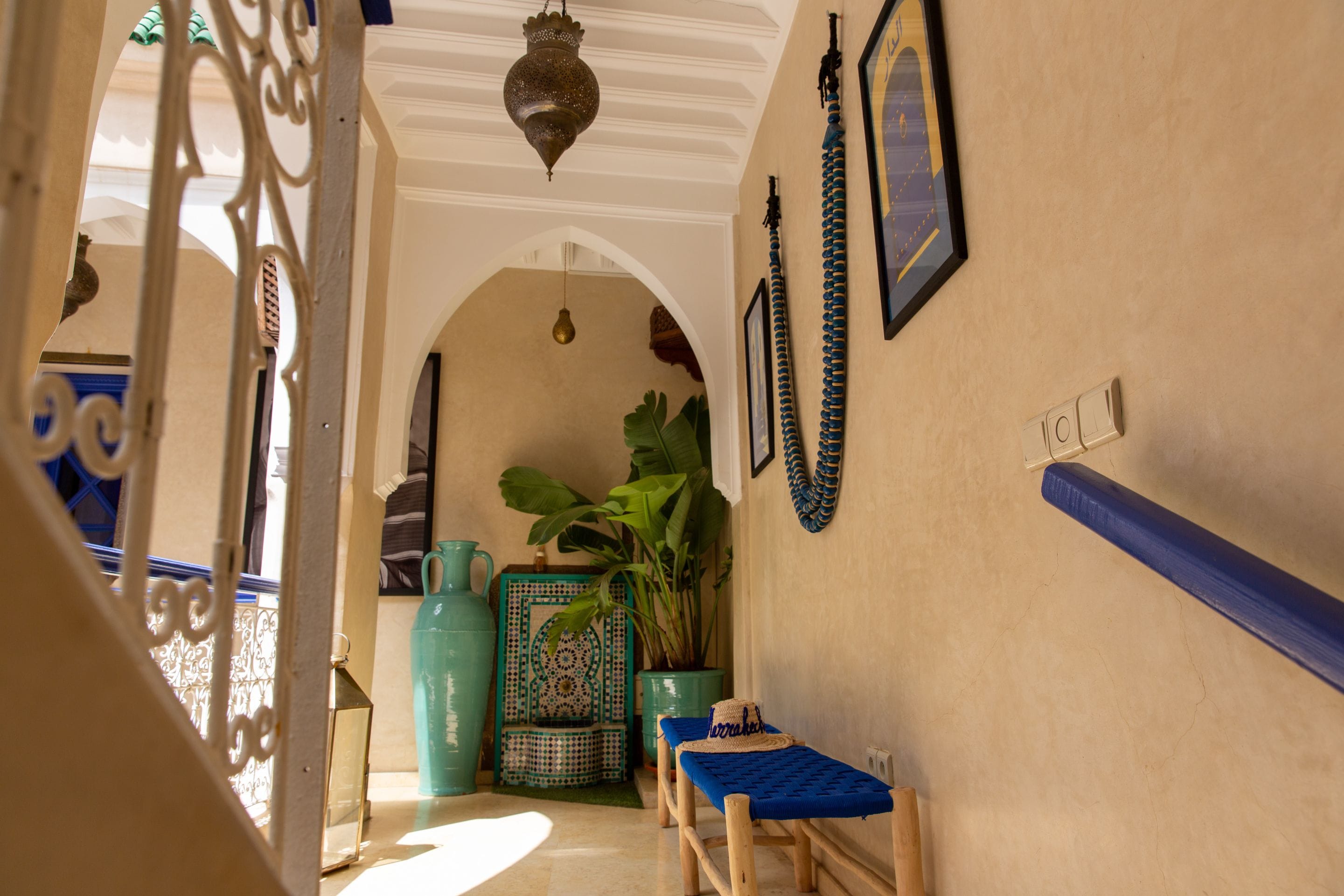 An interior corridor with a tiled wall, a hanging light fixture, a potted plant, and a small table with a blue cloth.