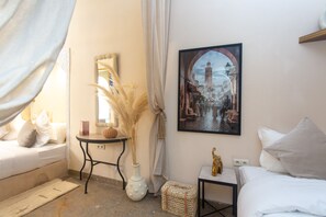 A room with a bed, a small table, a vase with dried plants, a framed picture on the wall, and a window with curtains. - Riad La Rose Orientale Marrakech (Marrakech)