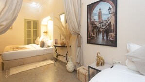 A hotel room with two beds, a large framed picture of a cityscape, a vase with dried plants, and a small table with a decorative item.