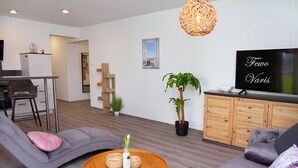 Una sala de estar moderna con un sofá, una mesa de centro, un televisor y una cocina al fondo.
