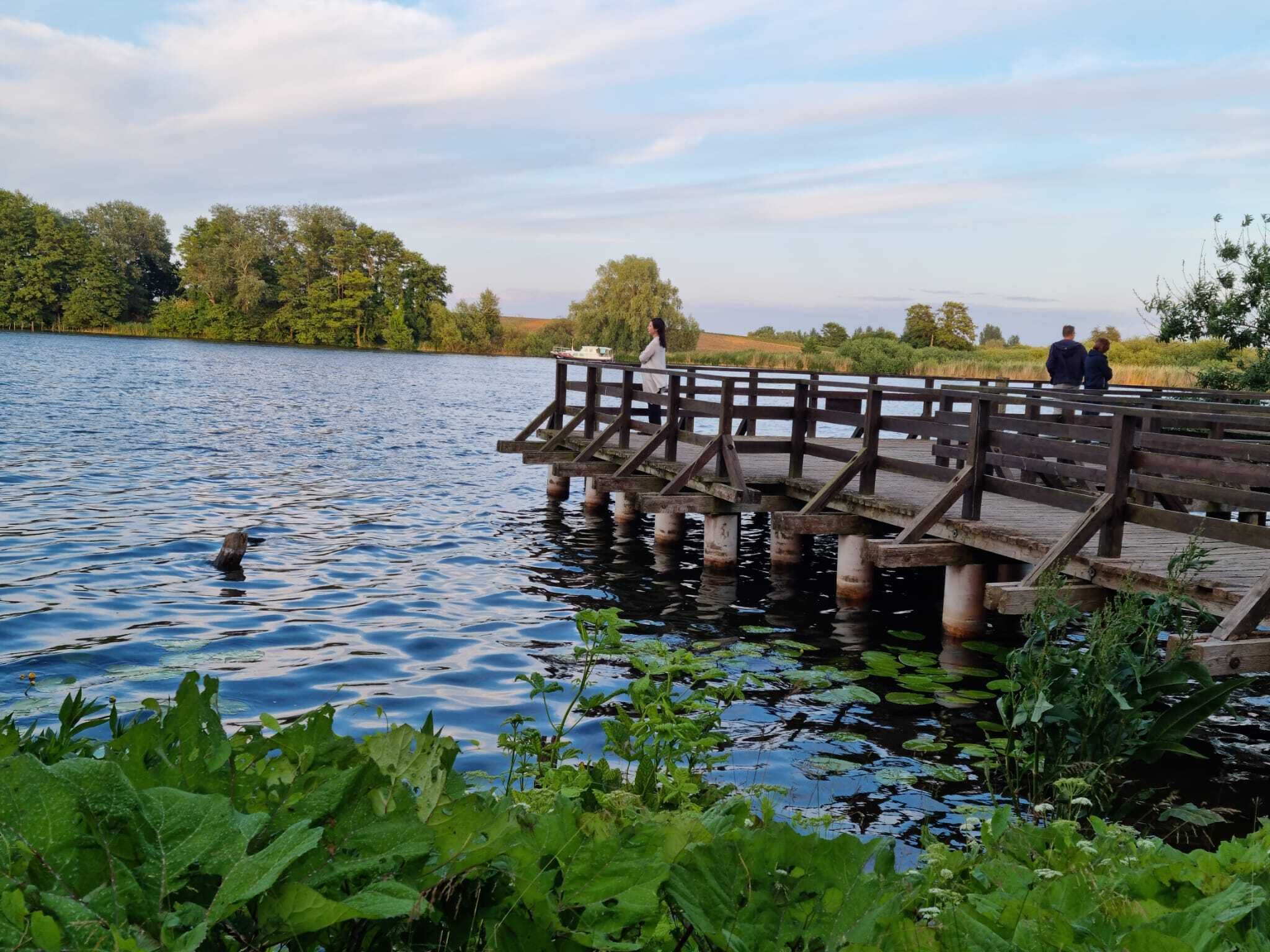 A wooden pier extending into a calm lake surrounded by lush greenery.