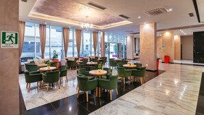 En hotellobby med grønne stole og borde, store vinduer og et synligt skilt med udgang.