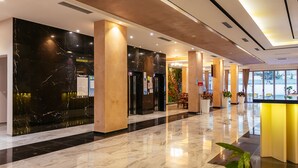 En moderne hotellobby med marmorgulv, en reception og et siddeområde med planter.