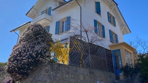 Un edificio de dos pisos con un muro de piedra al frente y una escalera a la derecha, bajo un cielo azul despejado.