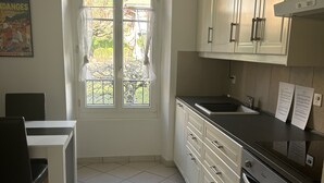 Una cocina con armarios blancos, encimera negra, una ventana con cortinas y suelo de baldosas.