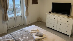 Un dormitorio con cama, cómoda, televisor y ventana con cortinas.