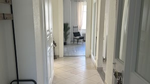 Un pasillo con piso de baldosas, un banco, una silla y una puerta adornada con un arreglo floral.